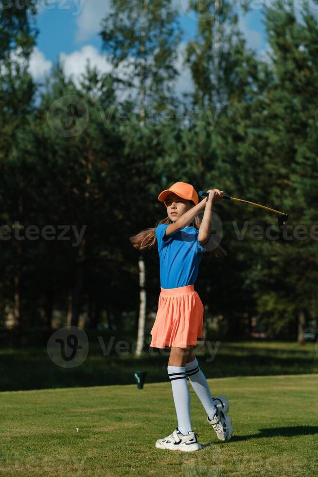 Young girl practicing golf swing on a sunny day at a green course surrounded by trees photo