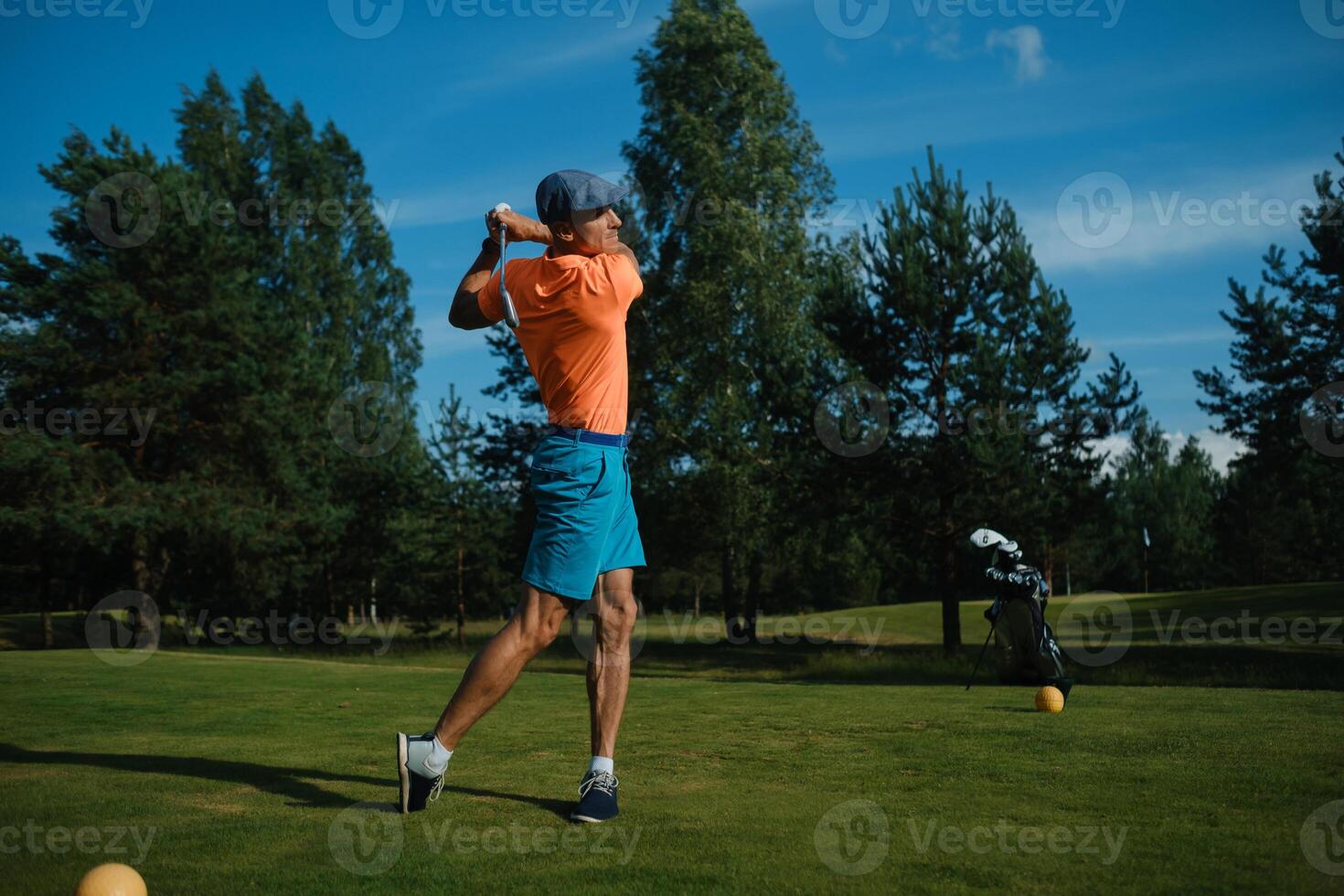 Golfer swinging a club on a sunny day at a lush green golf course surrounded by trees in mid-afternoon photo