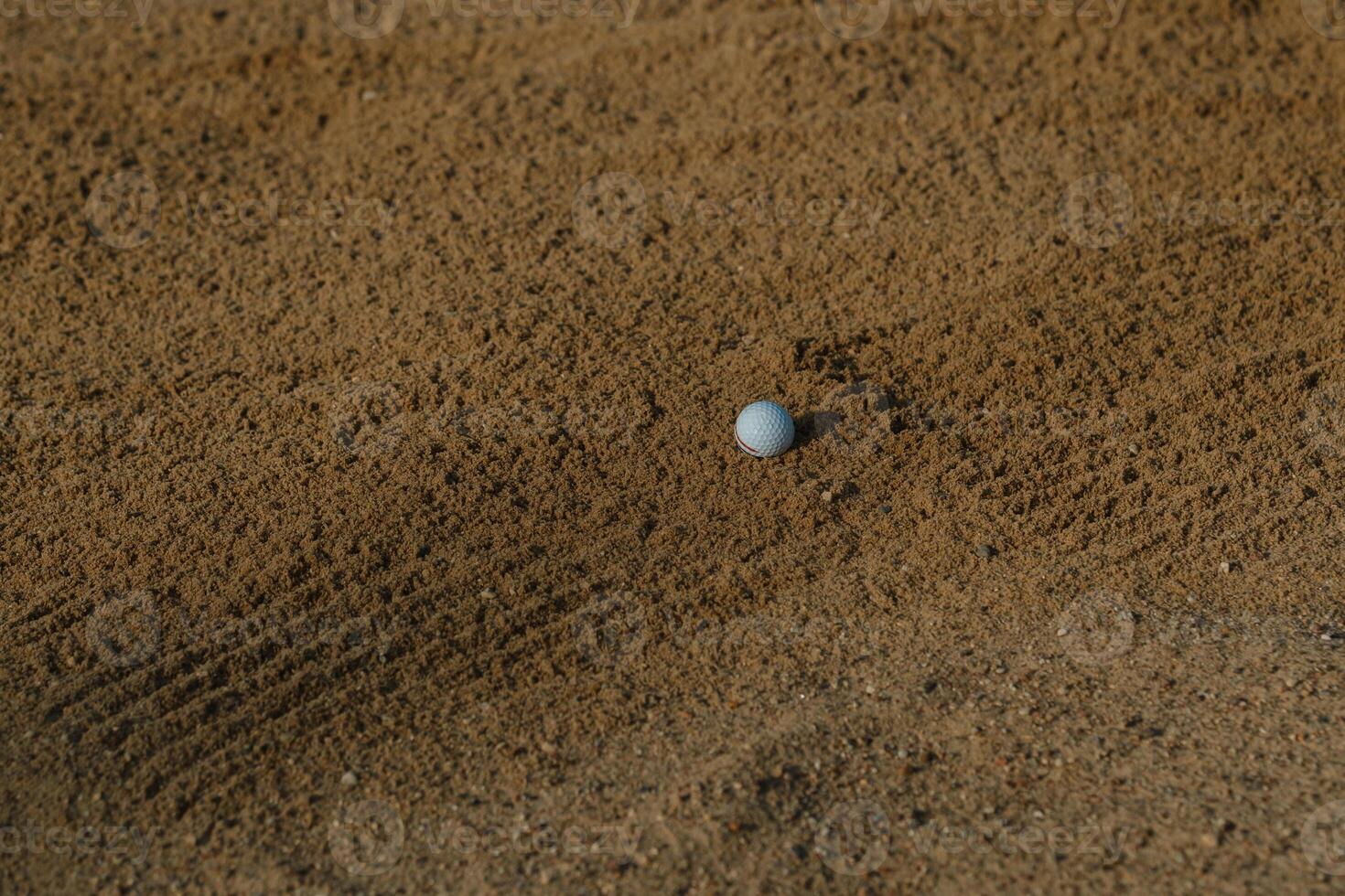 Golf ball resting on sand in a golf course bunker, highlighting the challenge players face during a round photo