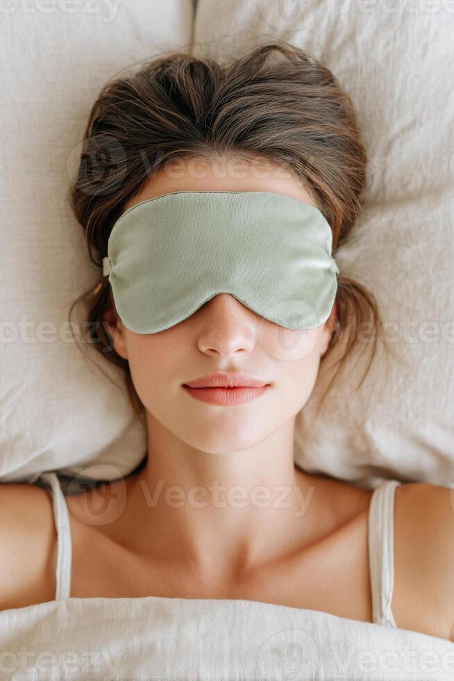 Woman with brown hair wearing a green sleep mask is lying on a soft pillow, surrounded by cozy bedding, creating a serene atmosphere for relaxation and rest photo