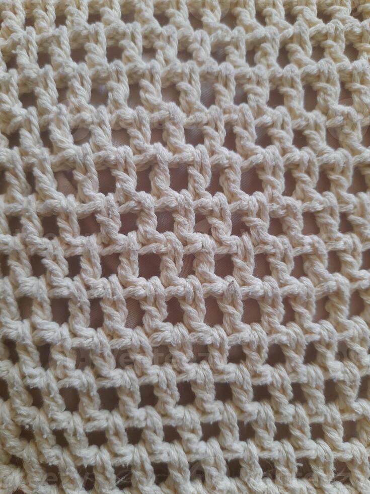 Close-up of a beige crochet net pattern with a square open weave, showcasing textured yarn and intricate looping design. photo