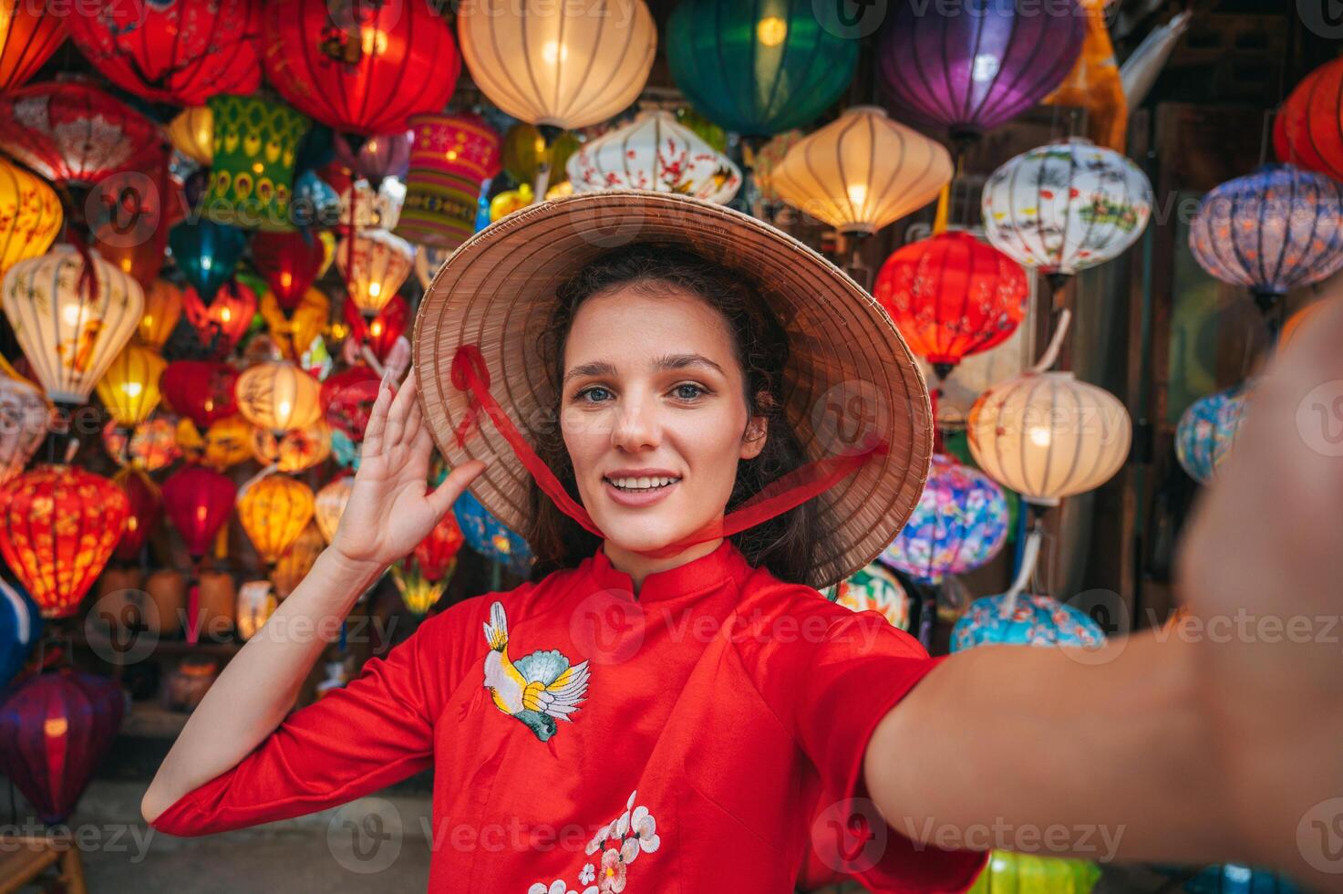 Selfie of a woman in traditional Vietnamese clothes and a conical Non La hat against the background of lanterns in the ancient city of Hoi An,. photo
