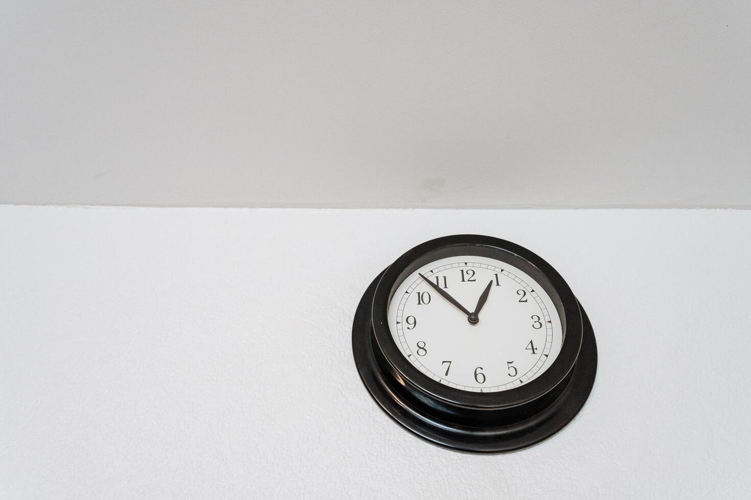 On a clean, white wall, there is a striking black clock beautifully hanging. This clock serves as a functional timepiece while also adding an artistic element to the decor photo