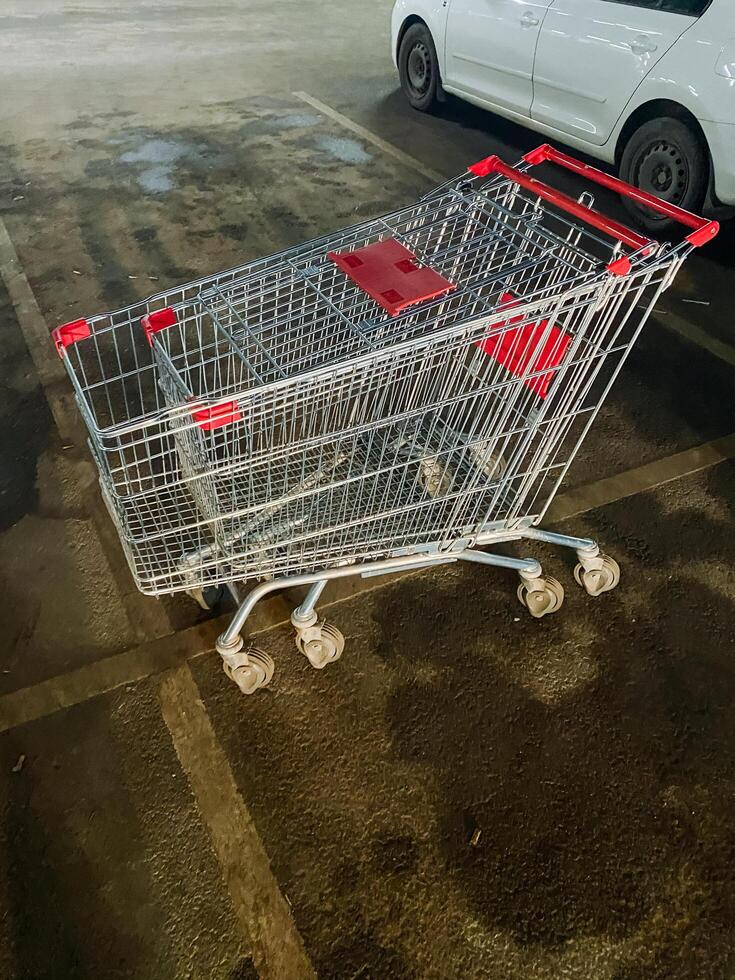 An empty shopping cart is parked next to a sleek white car in a busy parking lot, creating an unusual and intriguing scene amidst the diverse array of vehicles surrounding it photo