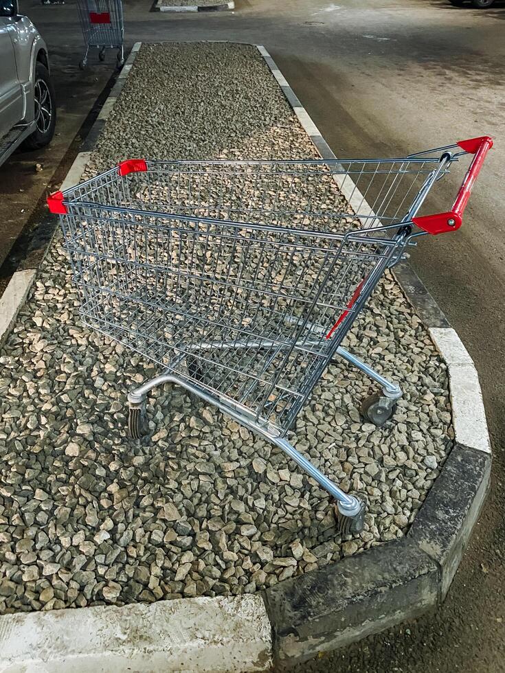 A shopping cart, made from materials such as steel and aluminum, is sitting idle on the side of the road, possibly abandoned or left behind for someone to pick up and use photo