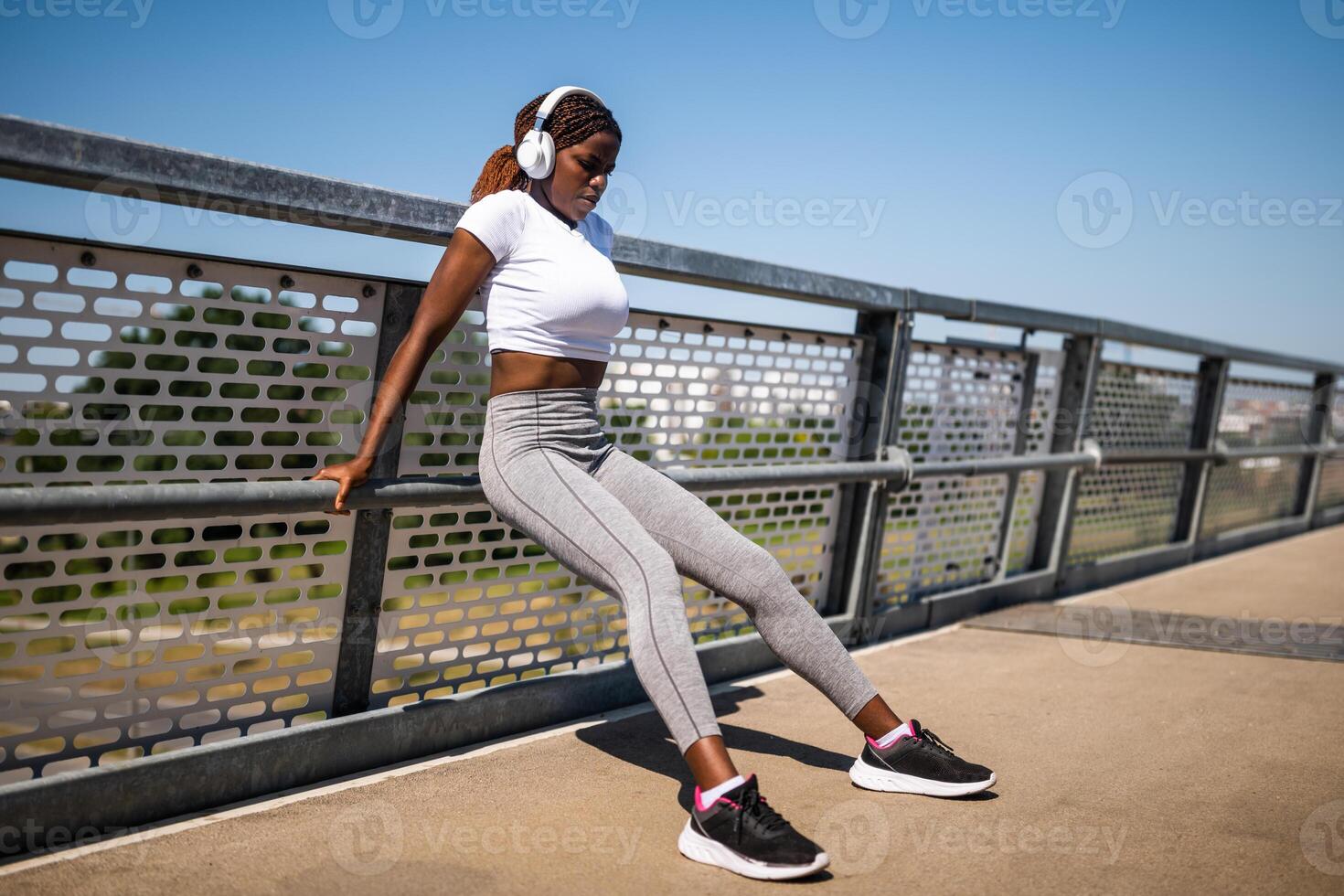 Outdoor shot of muscular African-American woman doing reverse push ups exercises with headphones, enjoying music while staying active. photo