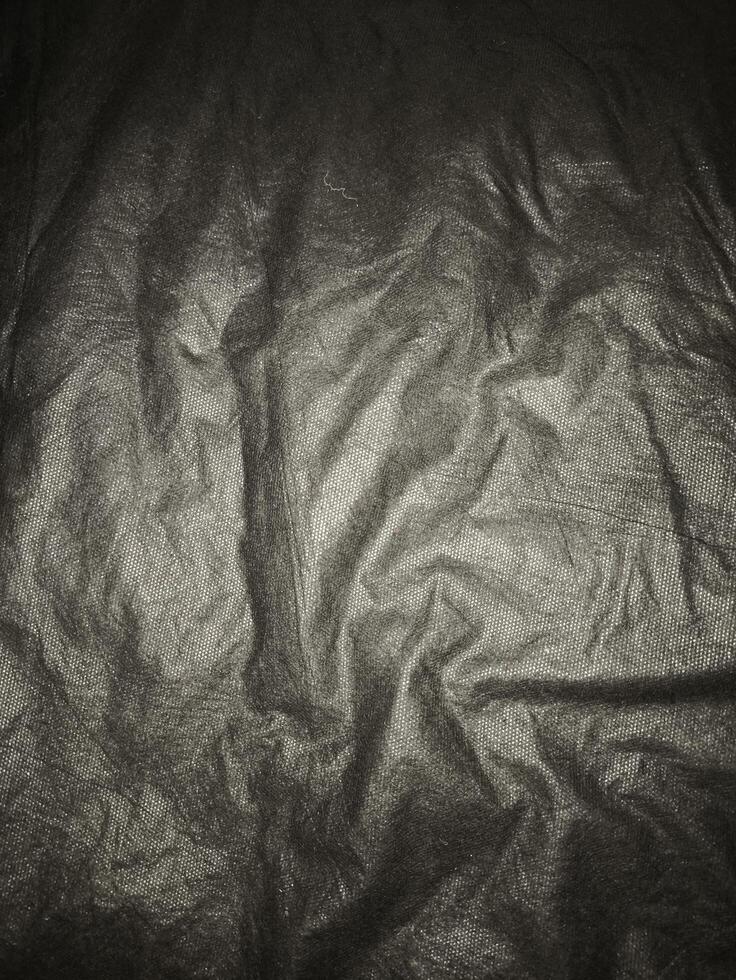 Wrinkled black synthetic fabric with subtle lighting and visible surface texture, ideal for background use in fashion, product display, or design elements that need dark textile feel. photo