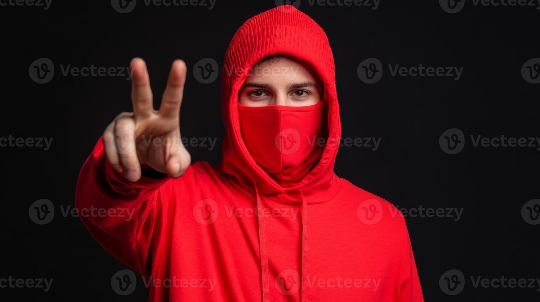 Young man in a red hoodie and mask showing peace sign against a dark background photo