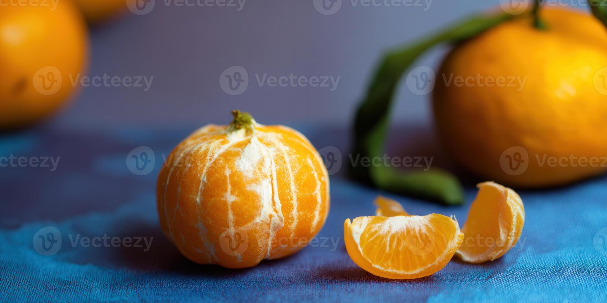 A vibrant close-up features a peeled mandarin orange and a segment on a blue surface. photo