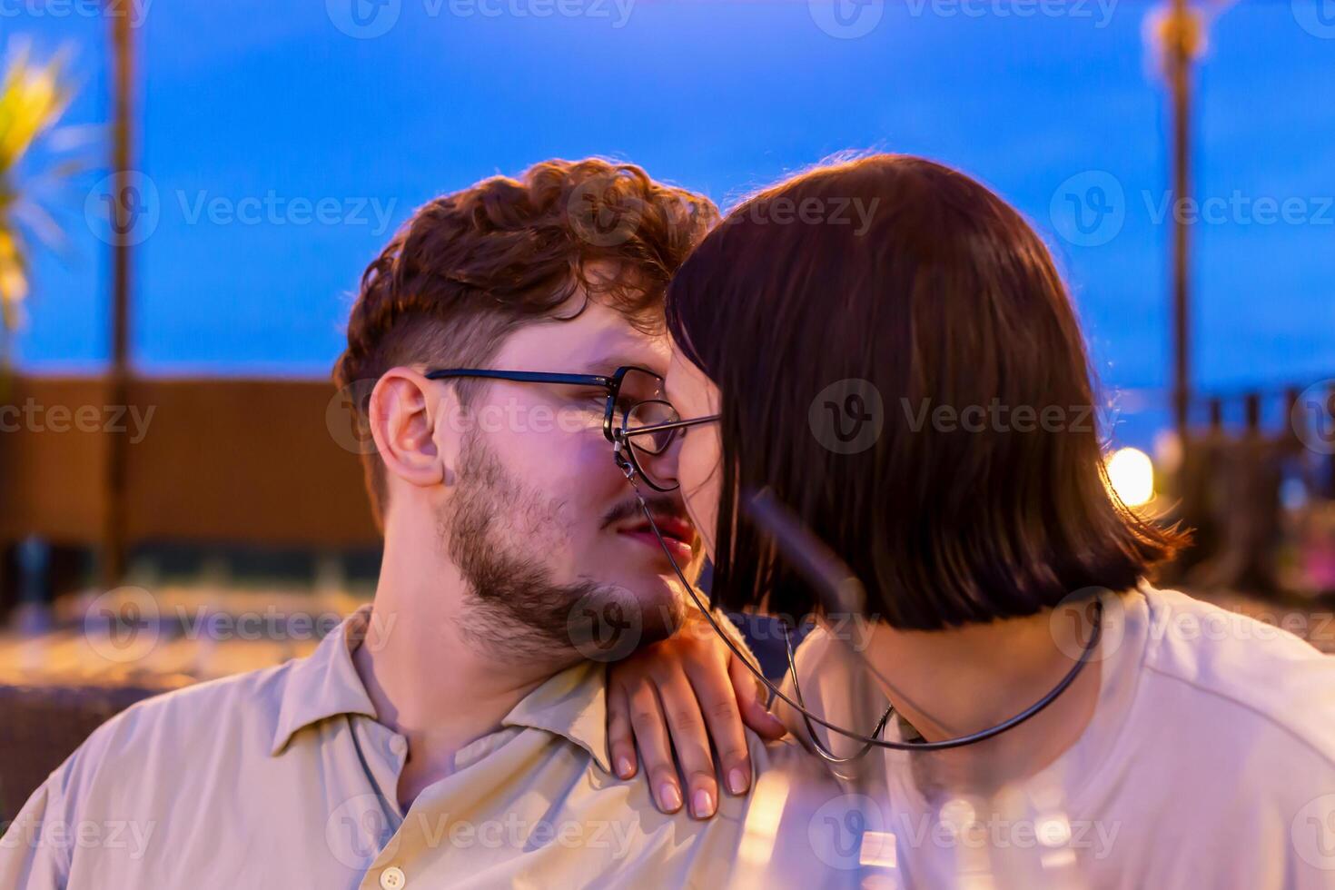 Romantic date on restaurant terrace at sunset. Romantic couple leaning close together, sharing kiss at outdoor cafe, with beautiful sunset backdrop creating warm and intimate atmosphere photo