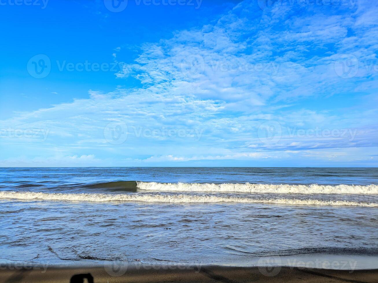 Serene Coastal Seascape Gentle Waves Under a Vast Blue Sky with Wispy Clouds. photo