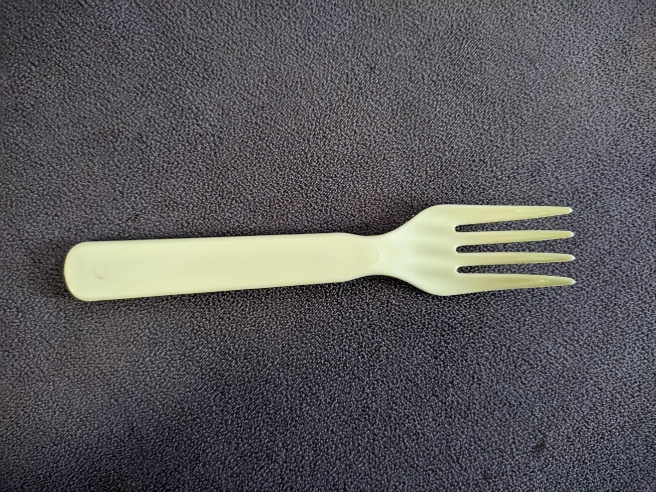 Yellow plastic fork on dark textured surface photo