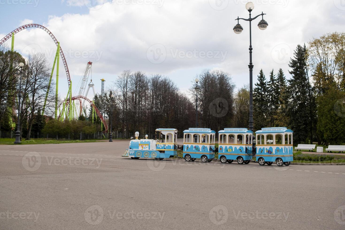Colorful Tourist Train Waiting Near Amusement Park Rides on a Cloudy Day in Spring photo