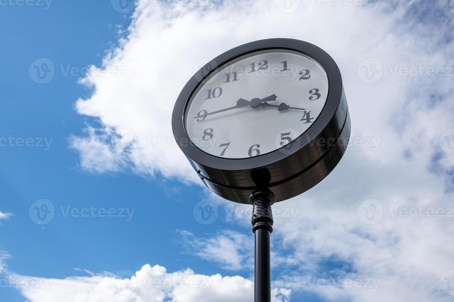 Vintage-style Clock Stands Tall Against a Bright Blue Sky With Fluffy White Clouds During a Sunny Afternoon photo