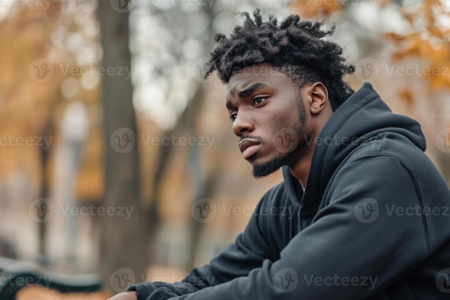 Young Black man contemplates life alone in a quiet park during autumn photo