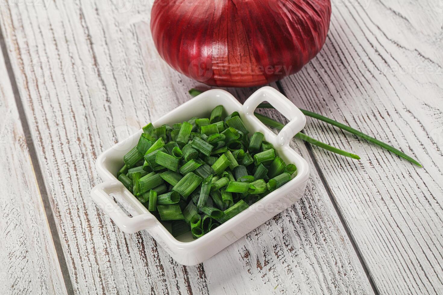 A white bowl with chopped green onions and a red onion photo