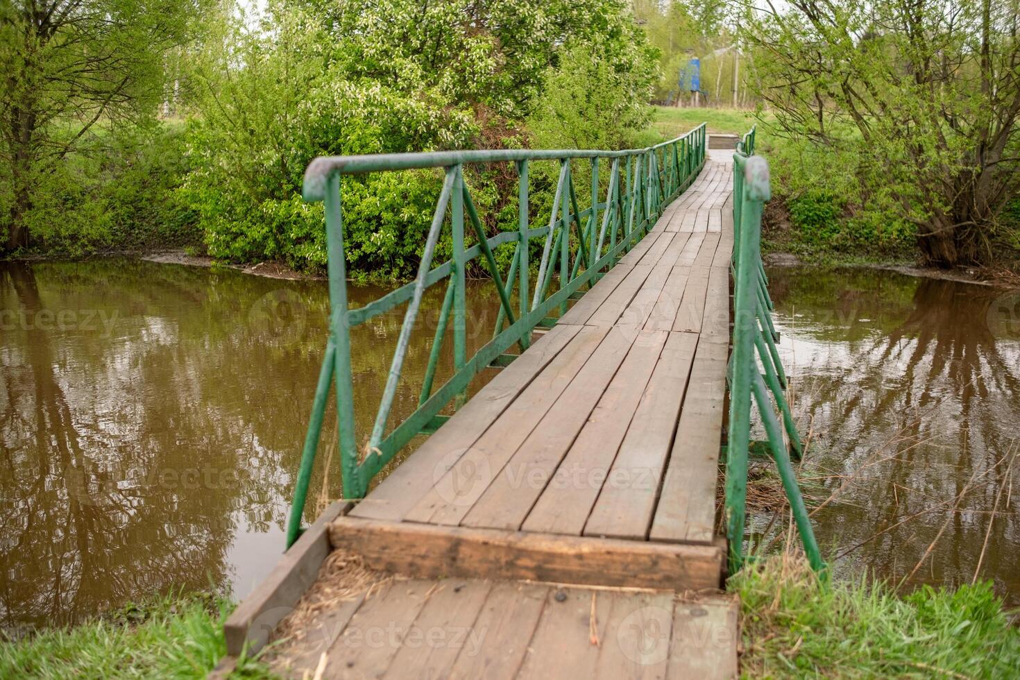Wooden Bridge Over a Peaceful Stream Surrounded by Greenery in a Serene Countryside Setting During Springtime photo