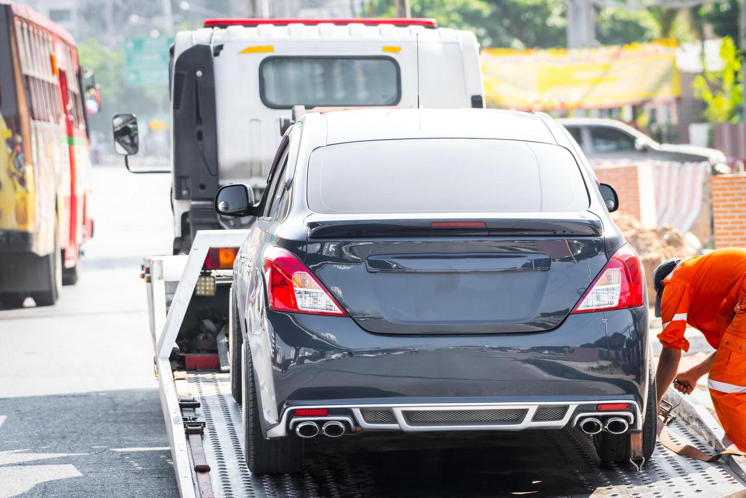 A man in an orange shirt is loading a car onto a truck photo