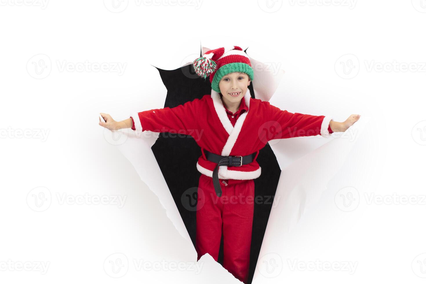 Child Santa Claus comes out of a hole in paper. A boy in a New Year's costume is smiling. Holiday surprise. Christmas holiday concept photo