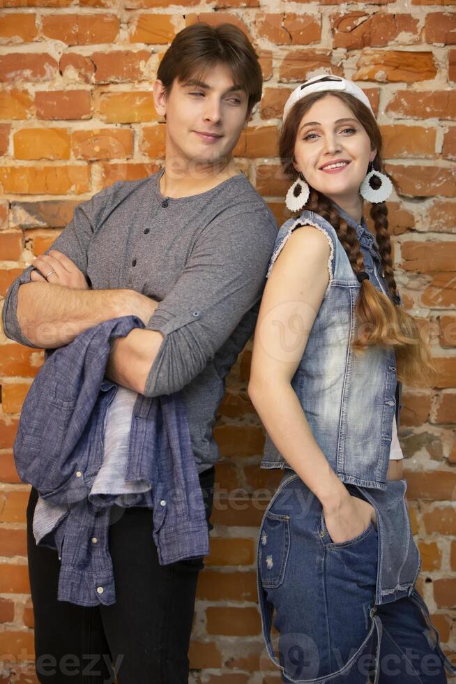 Vertical guy and girl are standing against a brick wall. Young couple in jeans clothes photo