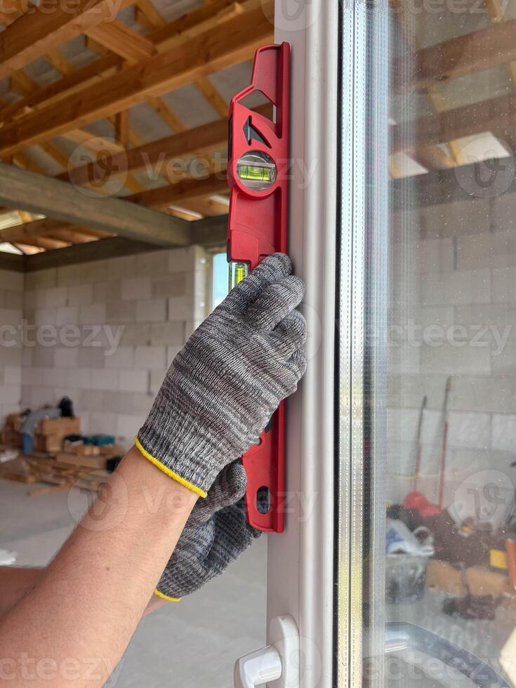 A worker wearing gloves and using a level checks the evenness of a new window at a construction site. photo