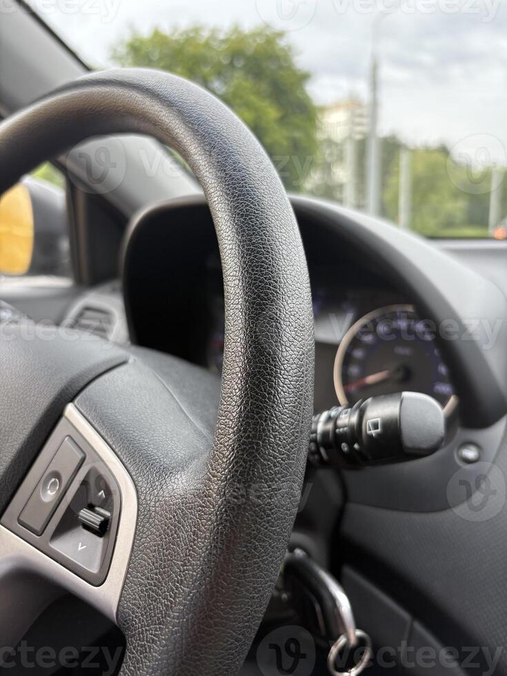 A vertical photo of a car steering wheel without hands while driving in the city.