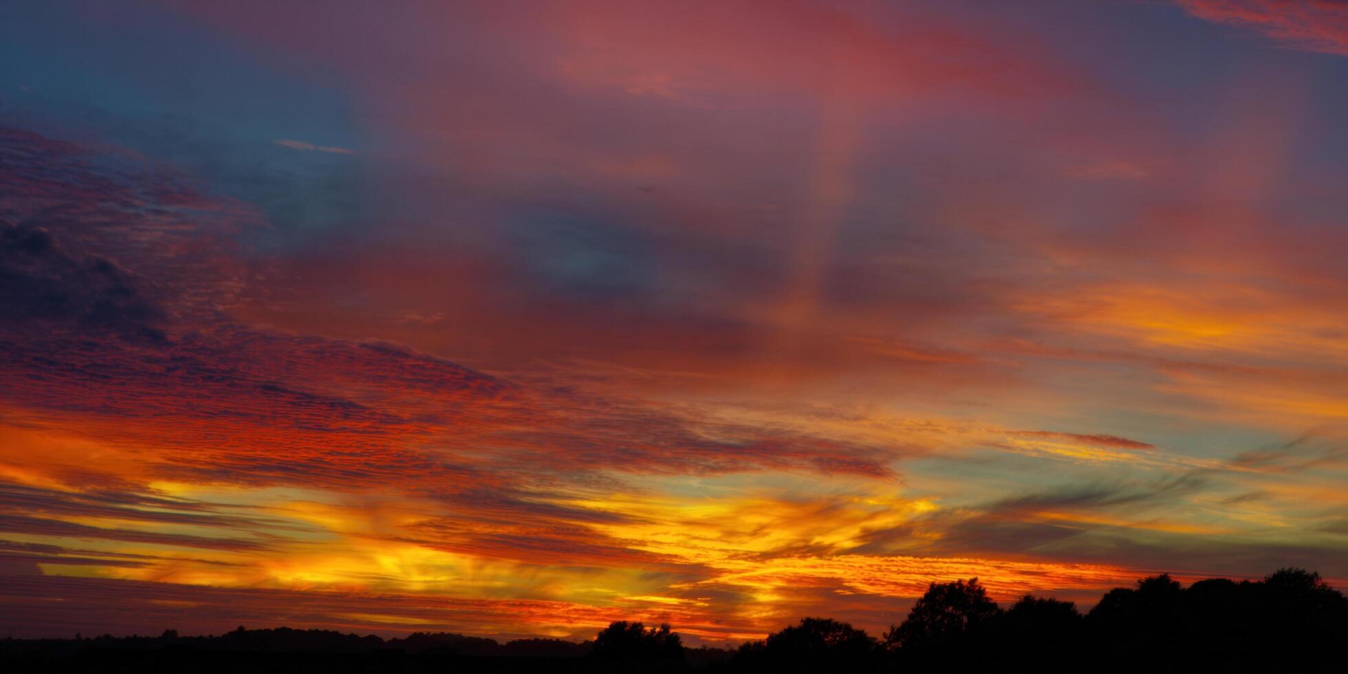 The sunset displays a colorful array of bright colors, and a silhouetted landscape. photo