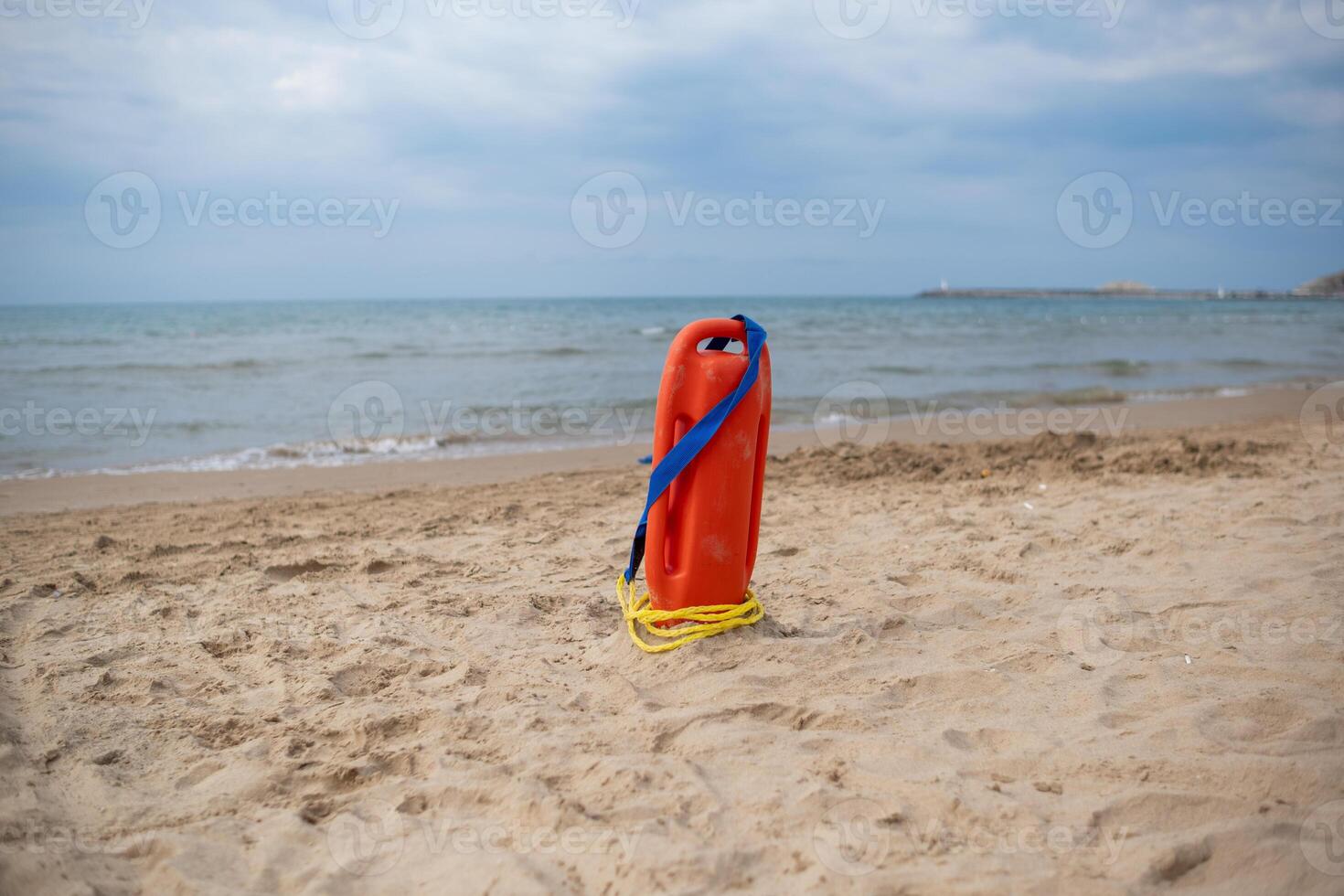 Lifeguard Buoy Stands on Sandy Beach Beside Calm Ocean Under Cloudy Sky During Early Evening photo
