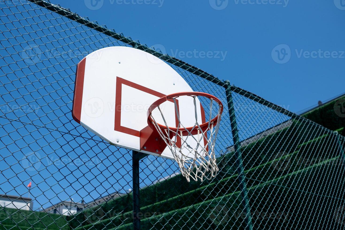 Basketball Hoop Attached to a Fence Under a Clear Blue Sky With a Few Clouds in the Background photo