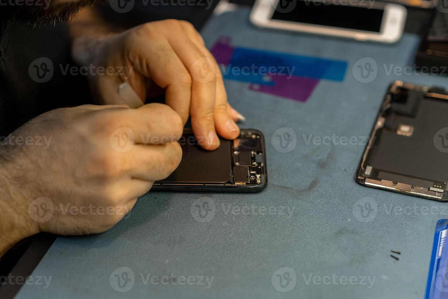 Expert Technician Repairs Smartphone Screen With Precision in a Busy Repair Shop During the Afternoon Hours photo