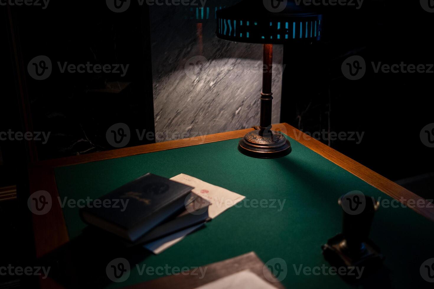 A Desk With a Green Felt Surface Illuminated by a Vintage Lamp Showcases Books and Papers in a Dimly Lit Room During the Night photo