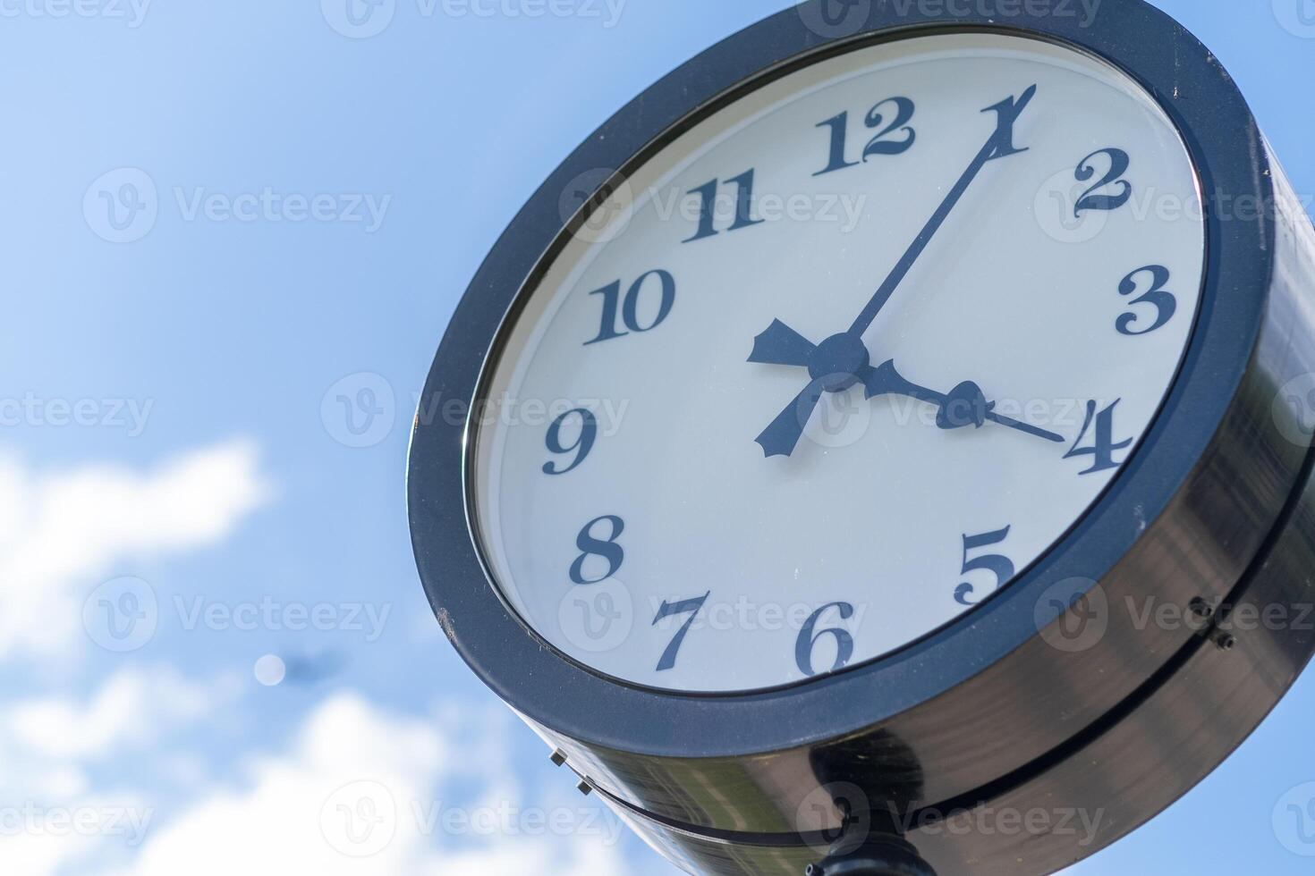 Classic Clock Under a Clear Blue Sky Near a Park, Showcasing the Time Just Before Four Oclock in the Afternoon photo