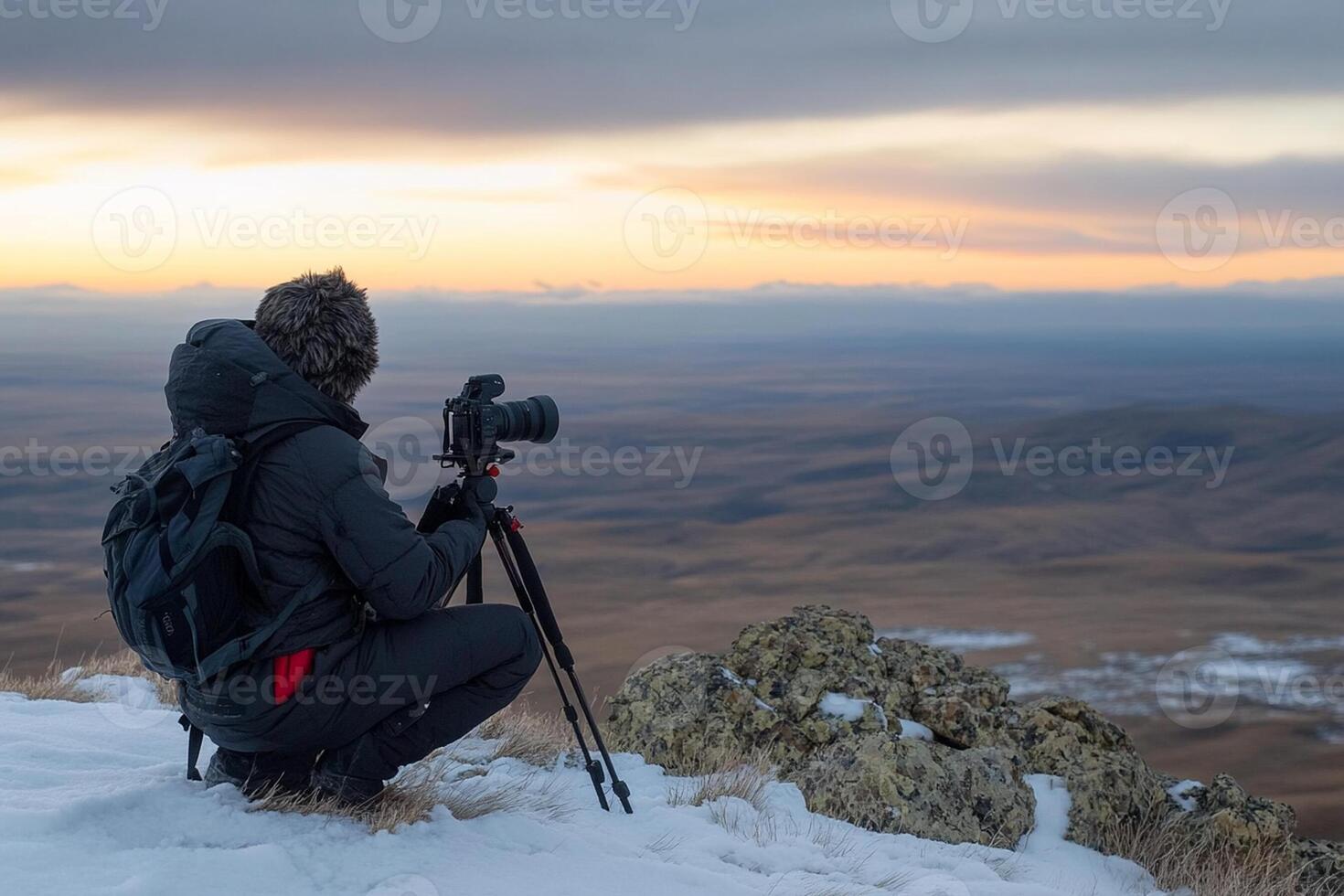 A man with a camera on a tripod sitting on top of a mountain photo