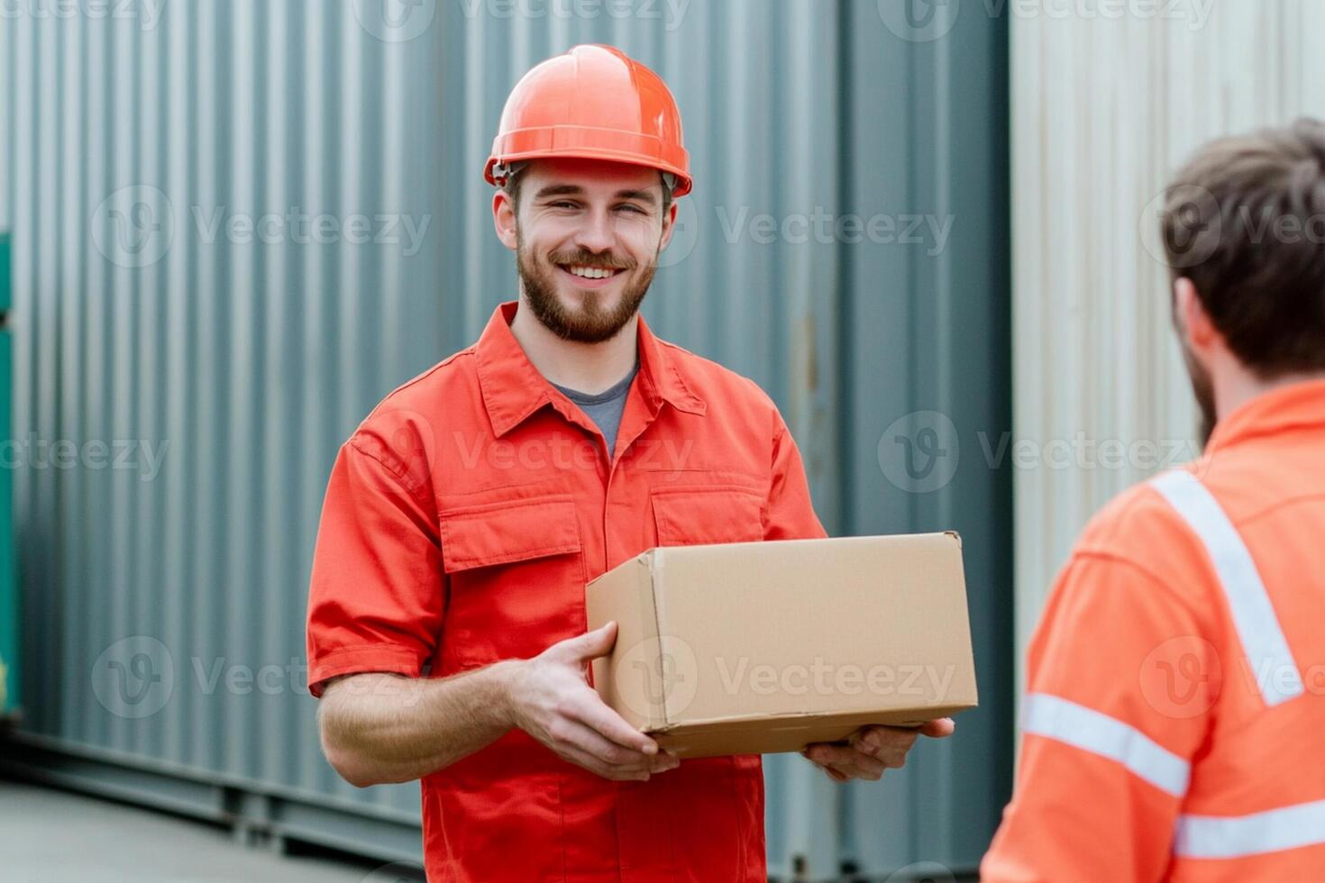 Two men in orange work clothes holding a box photo