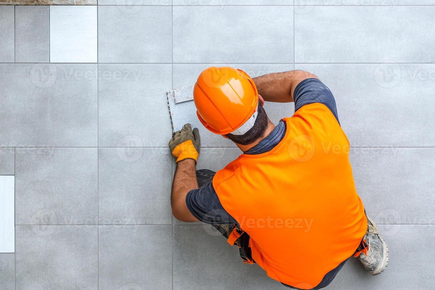 A man in an orange vest and hard hat is working on a tile floor photo