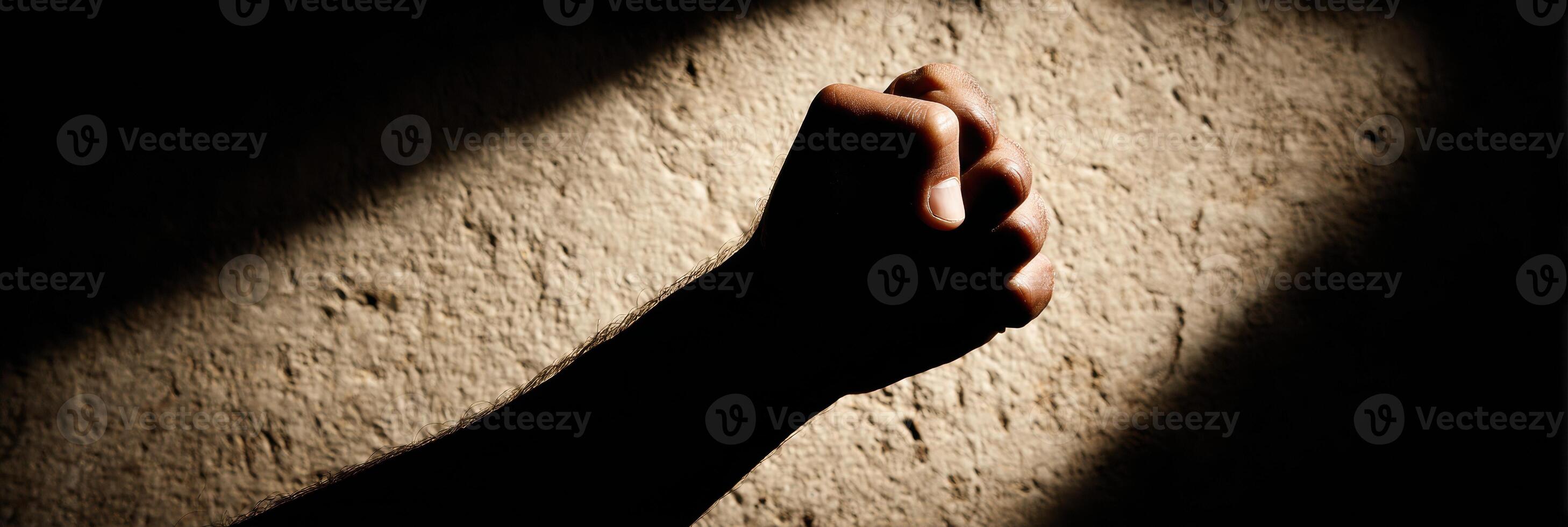 Clenched Fist Silhouette Casting a Long, Harsh Shadow on a Textured Surface During Late Afternoon Light photo