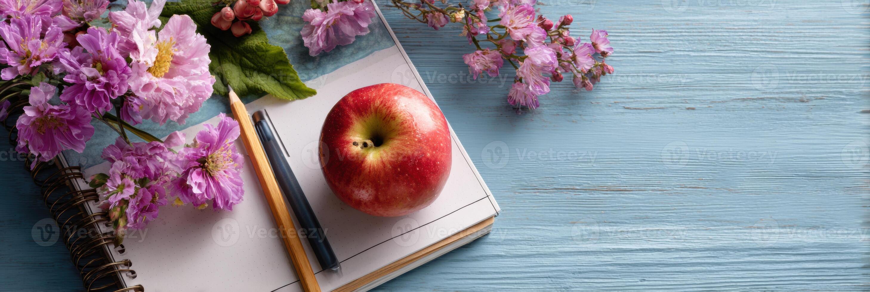 Flat Lay of a Teachers Desk Featuring a Notebook, Pen, Fresh Apple, and Colorful Flowers, Creating a Vibrant and Inviting Study Space photo