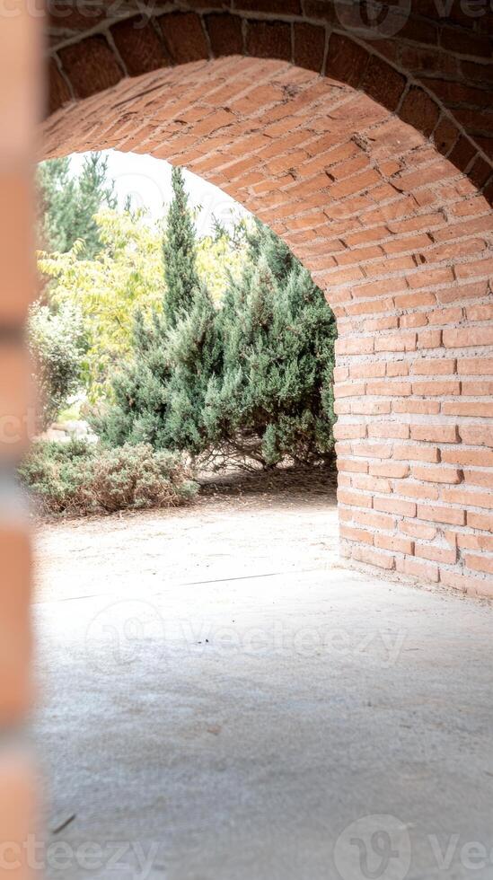 Sunlit brick archway framing a lush garden vista, inviting passage through ancient masonry into a tranquil natural outdoor space with vibrant green foliage. photo