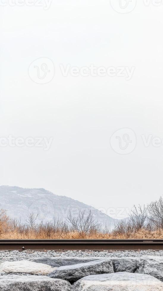 Scenic Railway Path Through Muted Winter Landscape Distant Mountains, Barren Vegetation, and Textured Rocks Under a Vast Sky photo