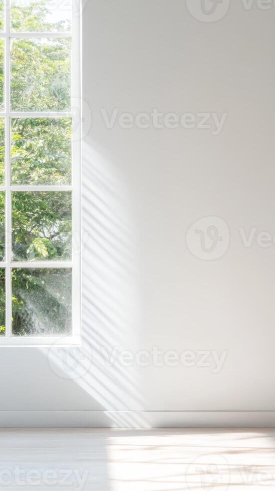 Bright, minimalist white room with large window showcasing natural light and dynamic shadows, offering a serene view of lush green trees and tranquil nature. photo