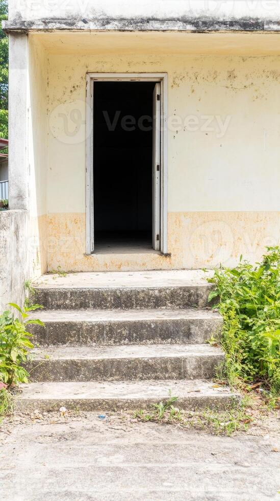 Weathered concrete steps lead to an open, dark doorway of an old, neglected building, evoking a sense of mystery and forgotten history. photo
