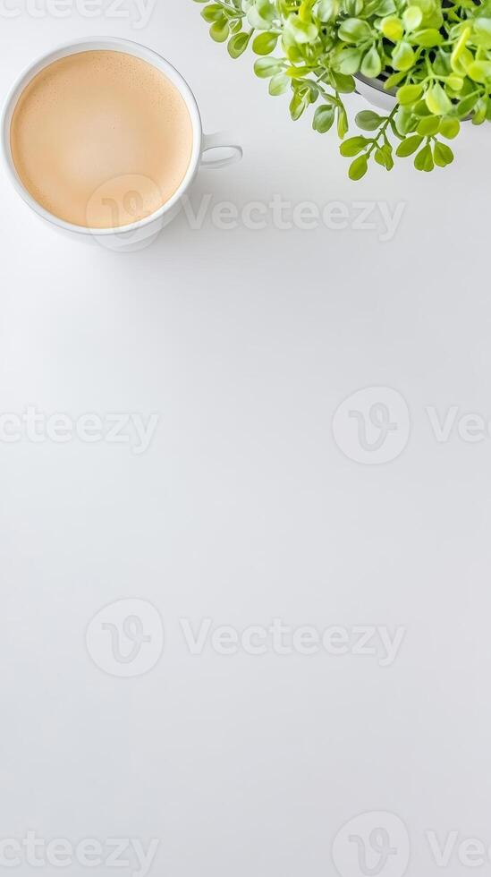 Overhead view of a creamy latte in a pristine white cup, artfully complemented by a vibrant green potted plant on a clean, bright surface. photo