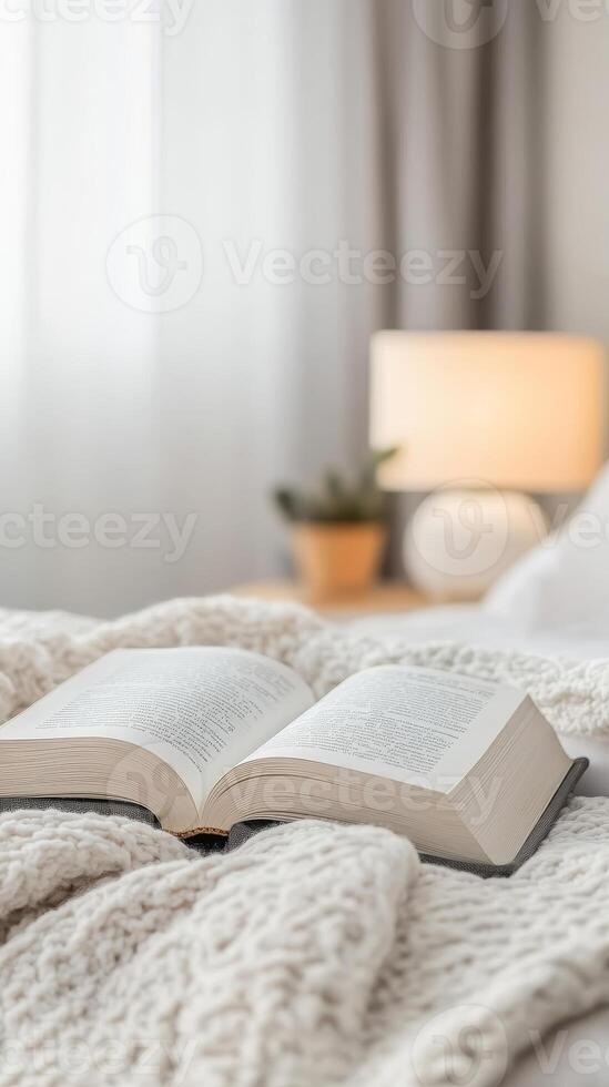 Open book resting on a soft, knitted blanket in a cozy bedroom, illuminated by a warm bedside lamp, perfect for relaxation and quiet reading moments. photo
