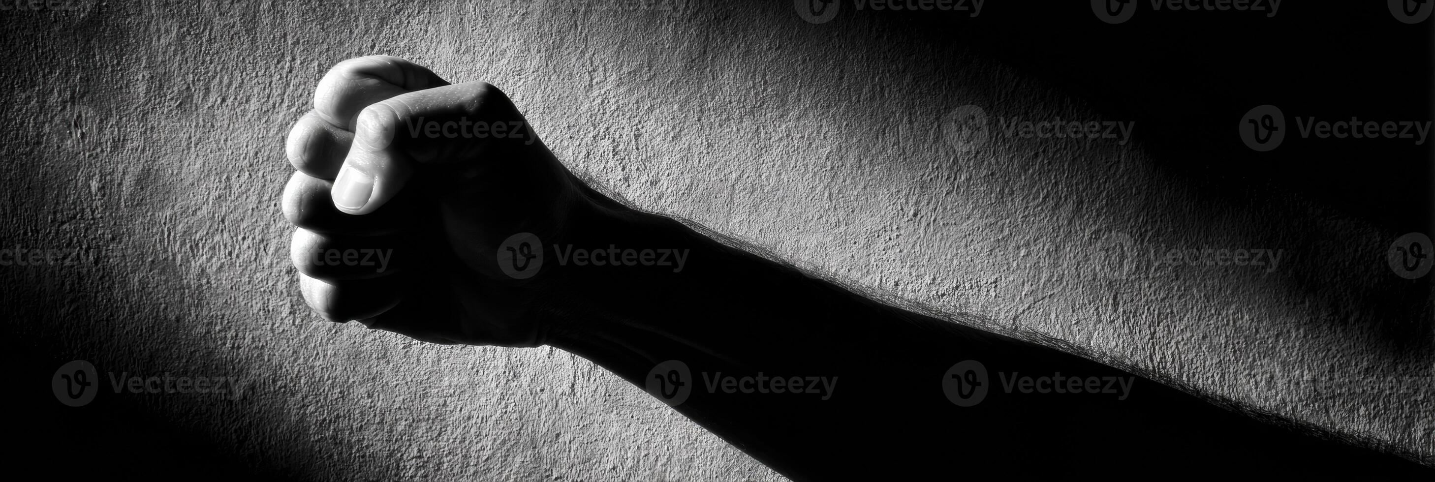 Clenched Fist Silhouette Casting a Long, Harsh Shadow on a Textured Wall During Dim Lighting photo