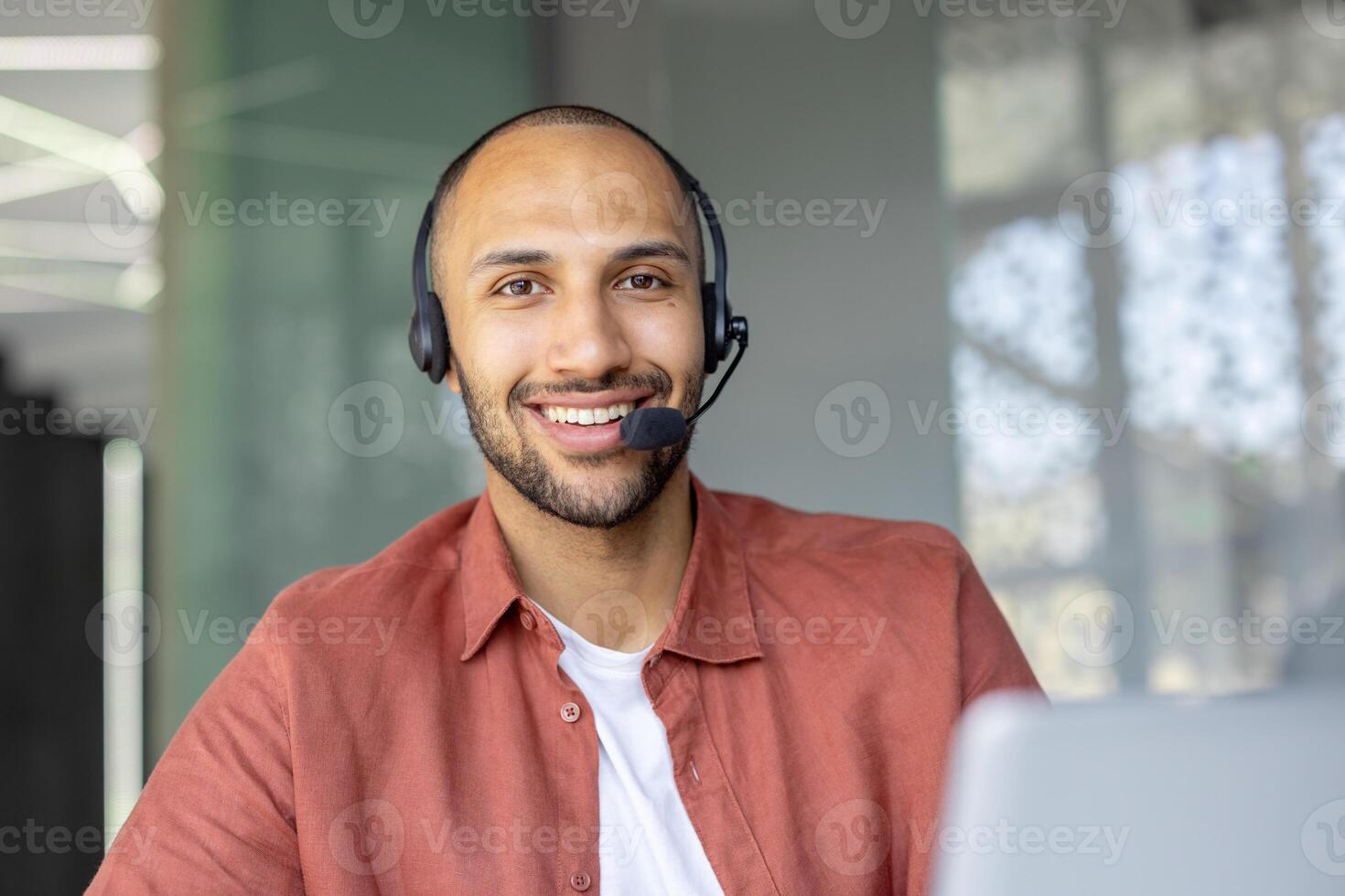 Smiling man wearing a headset, possibly a customer service representative, looking directly at the camera with a welcoming expression. photo