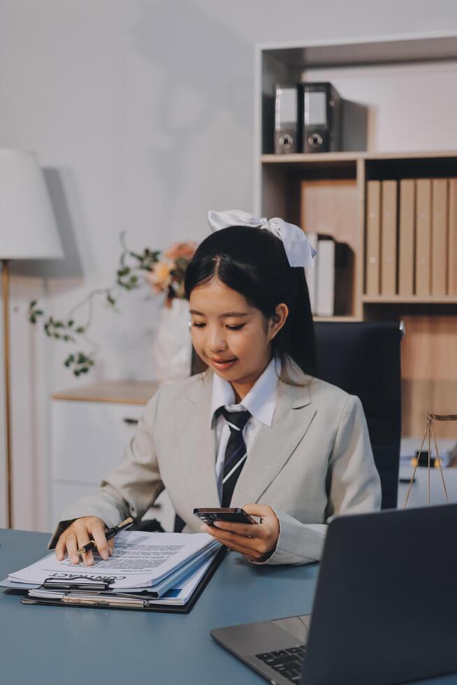 A woman in business attire sitting at a desk with a laptop and a phone photo