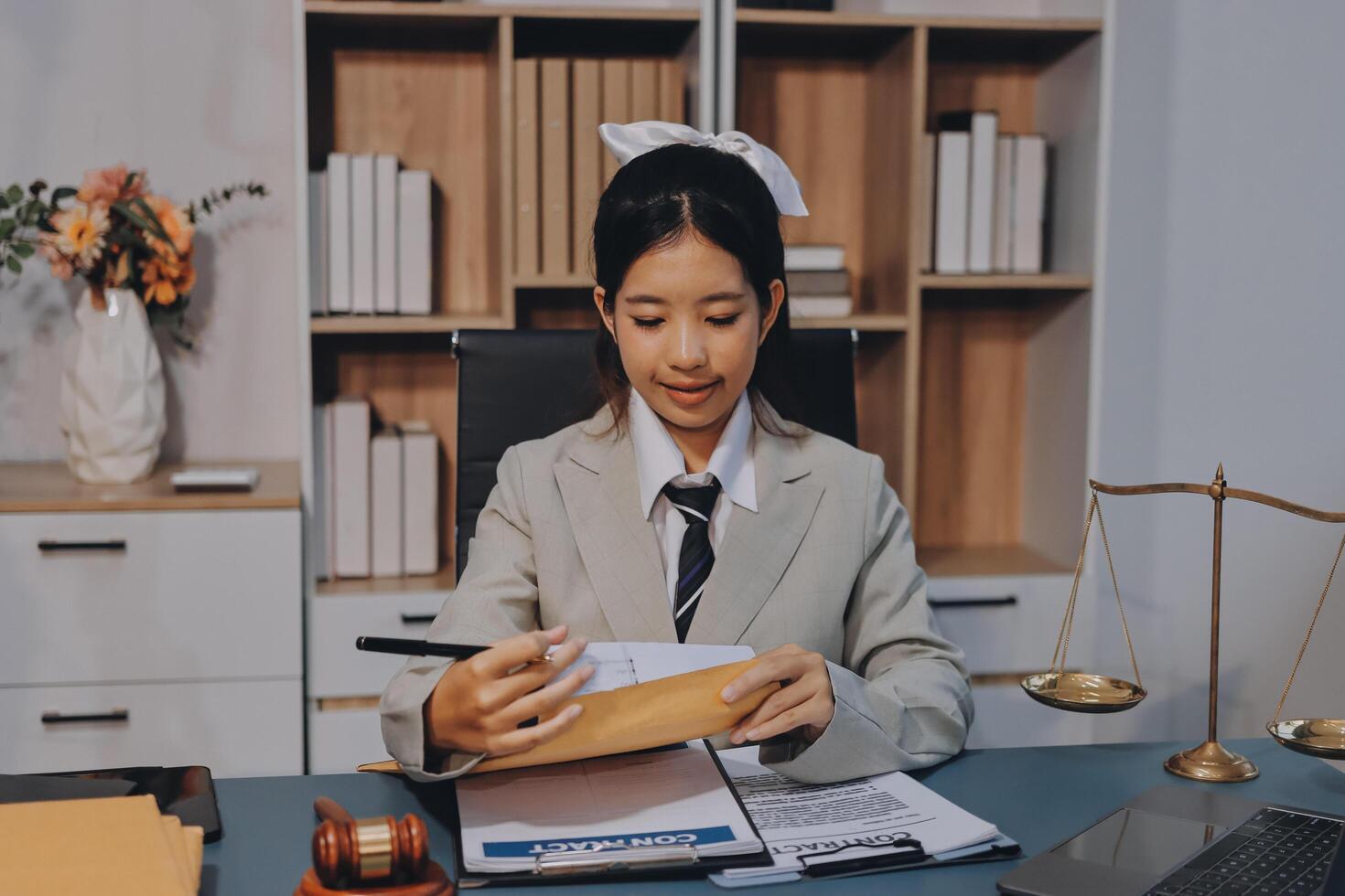 A young woman in a suit is sitting at a desk with a laptop and papers photo
