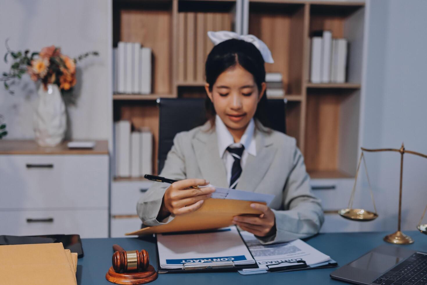 A woman in a suit is sitting at a desk with a laptop and papers photo