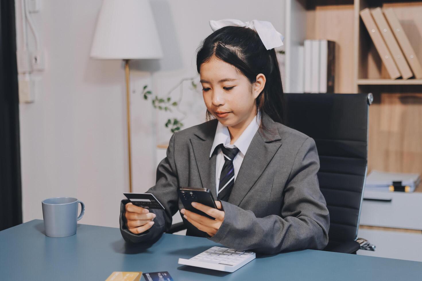 A girl in a business suit sitting at a desk with her phone photo