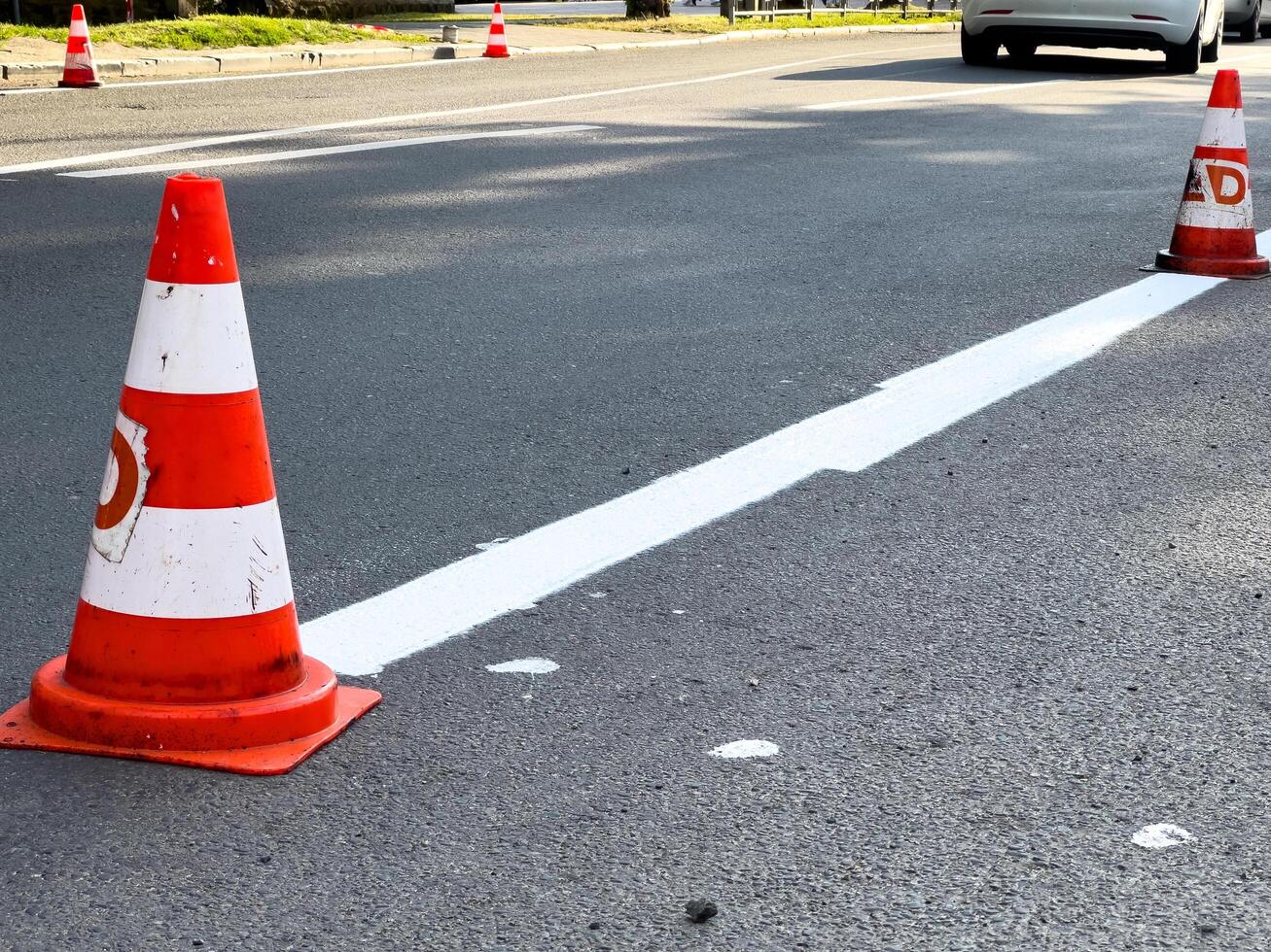 Road work area is outlined by traffic cones and freshly painted white lines on a busy street during daylight hours photo